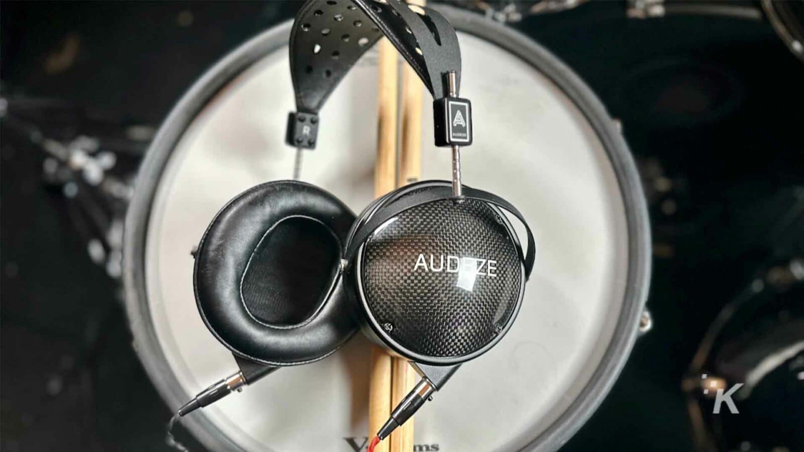 A drummer plays a percussion instrument while wearing headphones and listening to music through a loudspeaker connected to audio equipment with Audeze headphones.