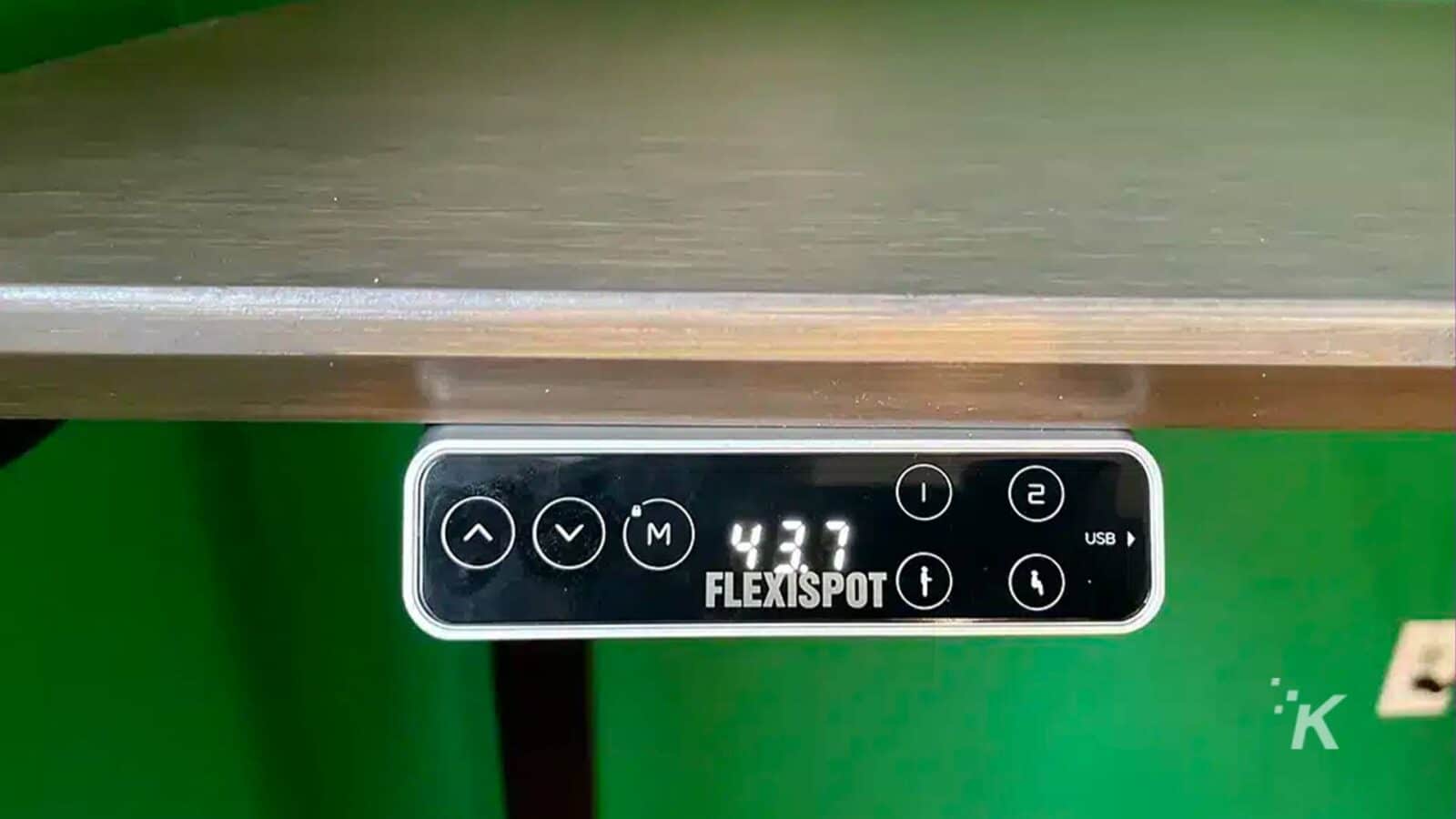 The image is showing a USB cable being connected to a FlexiSpot device. Full Text: - VM) 437 2 1 USB od FLEXISPOT K