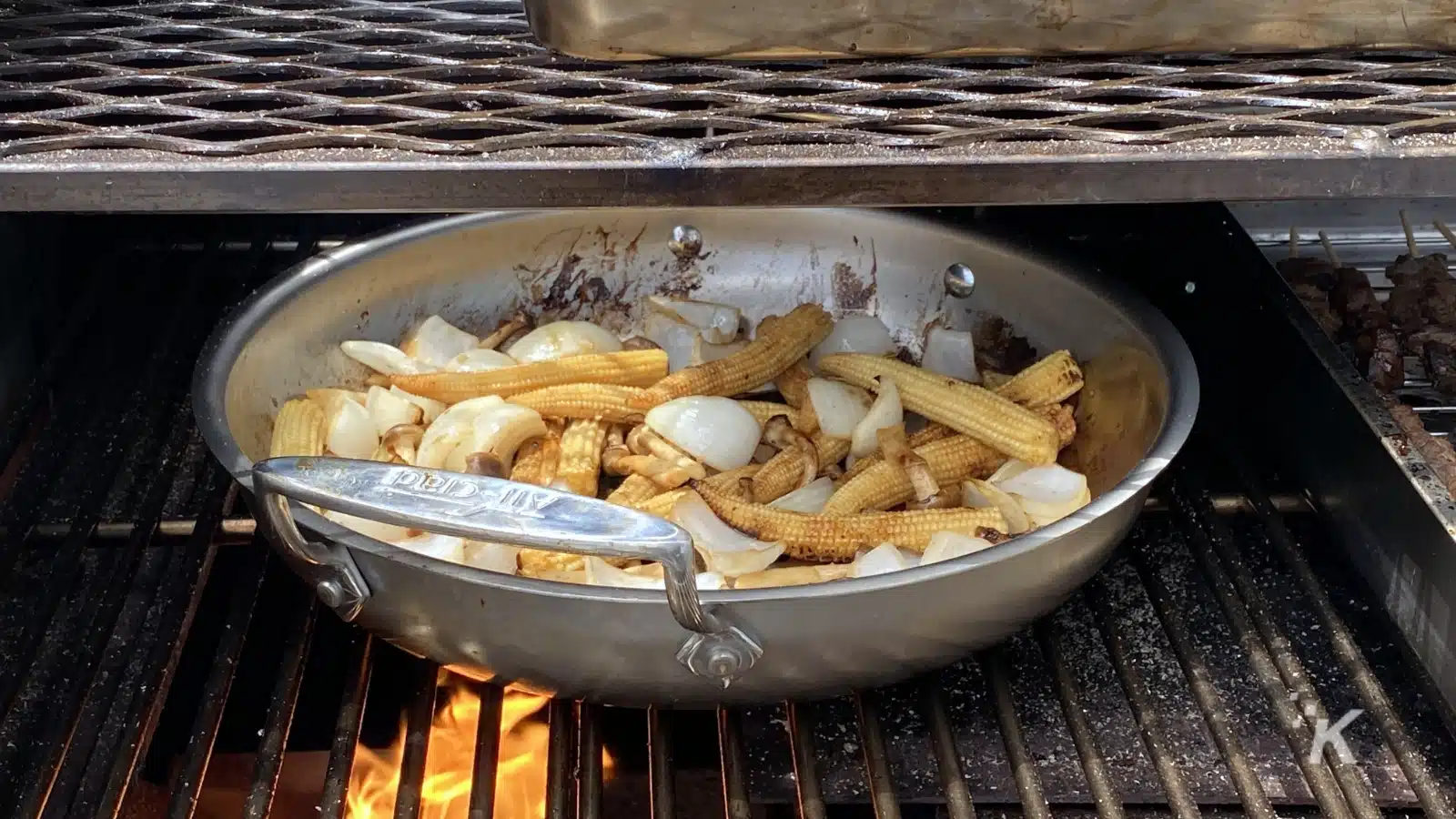 A cook is grilling chicken pieces and frying french fries in a pan of hot oil over a fast food restaurant's grill.